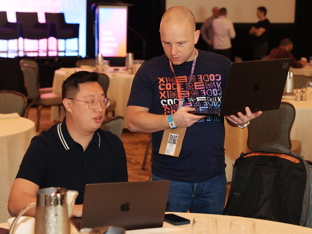 Two attendees working at a Hack Track table with the stage behind them